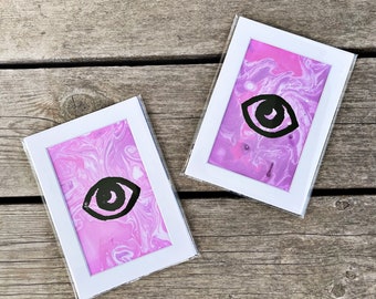 Può includere: Due stampe incorniciate con uno sfondo marmorizzato rosa e bianco e una grafica a occhio nero.