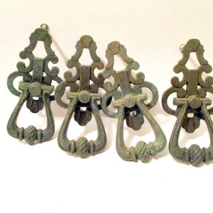 May include: Four antique brass cabinet door pulls with ornate designs. Each pull features a ring handle and a decorative top.