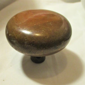 May include: A round, brass door knob with a dark brown finish. The knob has a slightly raised, smooth surface and a small, round base.