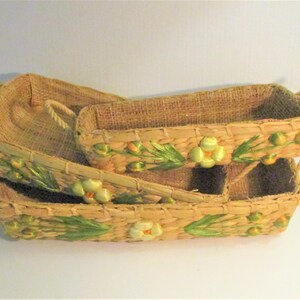 May include: Three woven baskets with green and yellow floral accents. The baskets are stacked on top of each other.