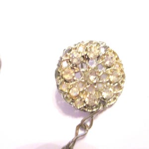 May include: Close-up of a pair of vintage earrings. Each earring features a round, ornate design encrusted with small, clear rhinestones. The earrings have a silver-toned metal setting and a delicate chain.