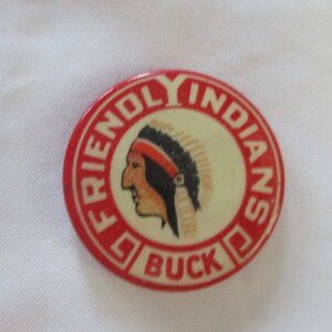 May include: A red and white button with the words "Friendly Indians" and "Buck" around the edge. A cartoon image of a Native American person wearing a headdress is in the center.