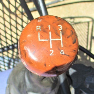 May include: Close-up of a brown, marbled gear shift knob with white numbers and letters indicating the gear positions: R, 1, 3, H, 2, 4.