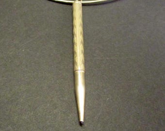 May include: A gold-toned necklace featuring a pendant shaped like a pen. The pen-shaped pendant has a textured design on the barrel and a pointed tip. The necklace chain is a thin, silver-colored wire.