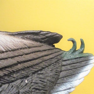 May include: Close-up of a duck decoy with brown and white feathers. The decoy has a green painted tail with two pointed tips.