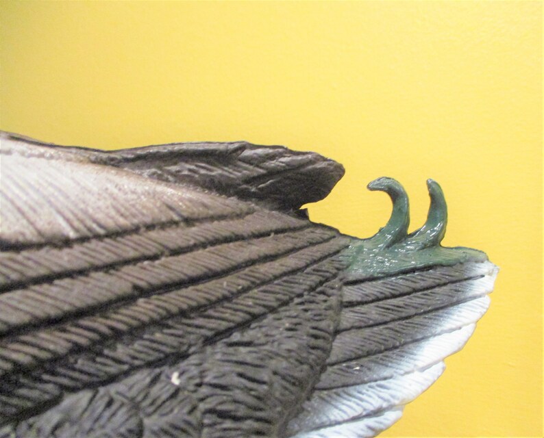 May include: Close-up of a duck decoy with brown and white feathers. The decoy has a green painted tail with two pointed tips.