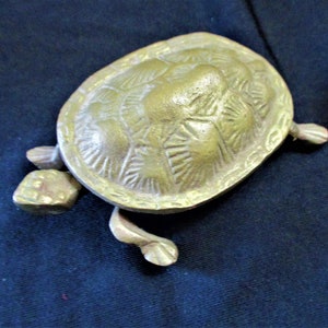 May include: A brass turtle figurine with a detailed shell design. The turtle is sitting on a dark blue surface.