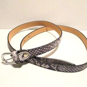 May include: A coiled belt with a snakeskin pattern in shades of gray and white. The belt has a silver-colored buckle and a light brown interior. This accessory is suitable for various outfits.