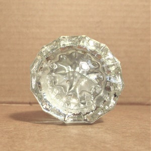 May include: A clear glass doorknob with a faceted design. The doorknob has a starburst pattern.