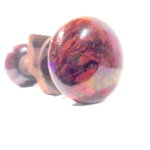 May include: A close-up of a red and brown ceramic knob with a swirl pattern. The knob is attached to a metal screw.