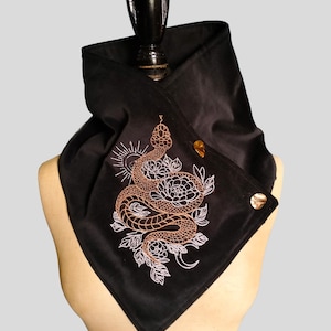 May include: Black velvet neck wrap featuring an embroidered design of a snake coiled around flowers and a sun. The embroidery is in copper and white. The wrap has two gold-coloured buttons.