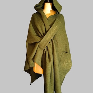 Puede incluir: Capa con capucha verde oliva, exhibida en un maniquí. La capa presenta una capucha grande, un bolsillo delantero y un diseño fluido. La tela tiene una apariencia suave y texturizada. La capa está hecha de un material suave.