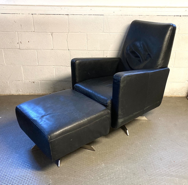 May include: A black leather armchair with a matching ottoman. Both pieces have a modern design with a swivel base.