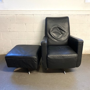 May include: A black leather armchair with a matching ottoman. The chair has a swivel base and the ottoman has a round base.
