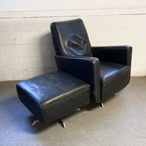 May include: A black leather armchair with a matching ottoman. Both pieces have a modern design with sleek lines and chrome legs.