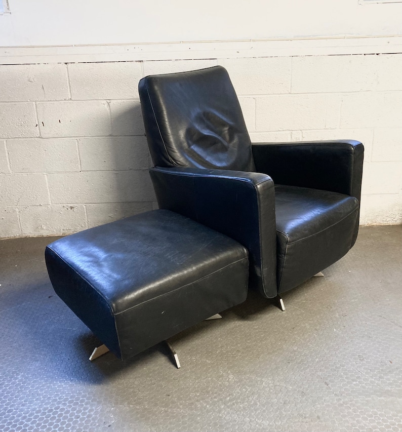 May include: A black leather armchair with a matching ottoman. Both pieces have a modern design with sleek lines and chrome legs.