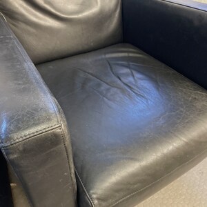 May include: A black leather armchair with a worn, distressed finish. The chair has a high back and wide arms, and the seat is slightly curved.