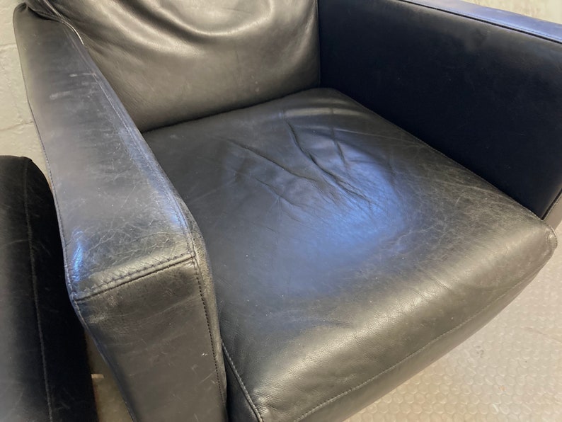May include: A black leather armchair with a worn, distressed finish. The chair has a high back and wide arms, and the seat is slightly curved.