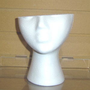 Puede incluir: Cabeza de maniquí de espuma blanca con cuello, utilizada para exhibir sombreros o pelucas.