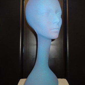 May include: A blue mannequin head with a long neck. The mannequin is made of a textured material and has a slightly faded blue color.