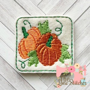 May include: Embroidered patch featuring two orange pumpkins with green stems and leaves. The pumpkins are surrounded by green vines and leaves. The patch is on a white background with a green border.