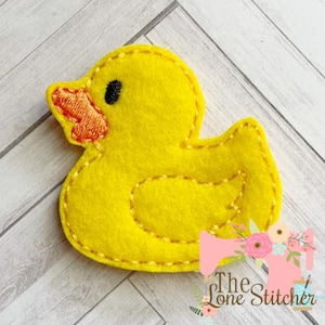 Puede incluir: Una aplicación de fieltro amarillo de un pato de goma con un ojo negro y un pico naranja.