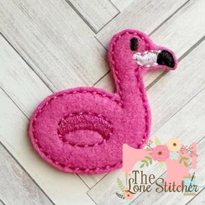 Könnte beinhalten: Rosa Filz-Applikation eines Flamingos mit einem weißen Auge und einem schwarzen Augendetail. Der Flamingo ist in Form eines aufblasbaren Pool-Schwimmringes.