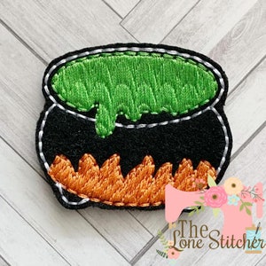 May include: A black cauldron with green bubbling liquid and orange flames. The cauldron is embroidered with a white outline.