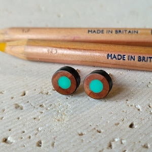 Op de afbeelding: Een paar houten oorbellen met een turquoise groene cirkel in het midden. De oorbellen zijn gemaakt van hout en hebben een zwarte rand.