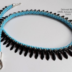 Pode incluir: Um colar de contas pretas e turquesa com um fecho prateado. O colar apresenta uma franja de contas pretas.