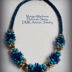 May include: A blue and gold beaded necklace with a cluster of blue beads at each end. The necklace is called "Mango Madness" by Deborah Shipp, DMK Artisan Jewelry.