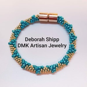 May include: A turquoise and gold beaded bracelet with a magnetic clasp. The bracelet is made with small, round beads and has a twisted design. The text "Deborah Shipp DMK Artisan Jewelry" is visible in the centre of the image.
