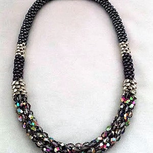 Op de afbeelding: Een zwarte en zilveren kralenketting met een magneetsluiting. De kralen zijn in een spiraalvorm gerangschikt en hebben iriserende accenten.