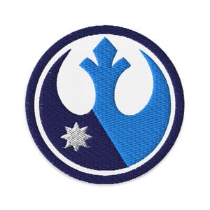 Könnte beinhalten: Gestickter Aufnäher mit einem kreisförmigen Design in Blau und Weiß. Der Aufnäher hat einen dunkelblauen Außenring, einen weißen Innenring und ein zentrales Emblem mit einem stilisierten Stern und einer vogelartigen Form in Blautönen.