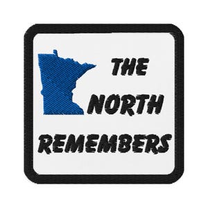 May include: Embroidered patch with a white background and a black border. The patch features a blue outline of the state of Minnesota and the text "THE NORTH REMEMBERS" in black.