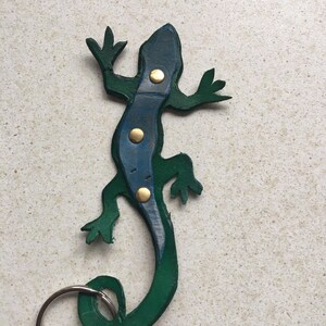 May include: A green and blue leather lizard keyring with gold accents. The lizard's tail is curled into a circle, forming a key ring.
