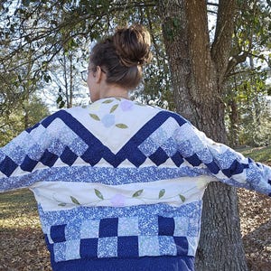 Pode incluir: Uma jaqueta acolchoada azul e branca com um design floral. A jaqueta tem um decote em V e mangas compridas.
