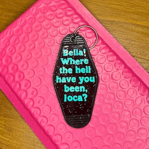 May include: A black hotel key tag with the text "Bella! Where the hell have you been, loca?" in turquoise. The key tag is on a pink bubble mailer.