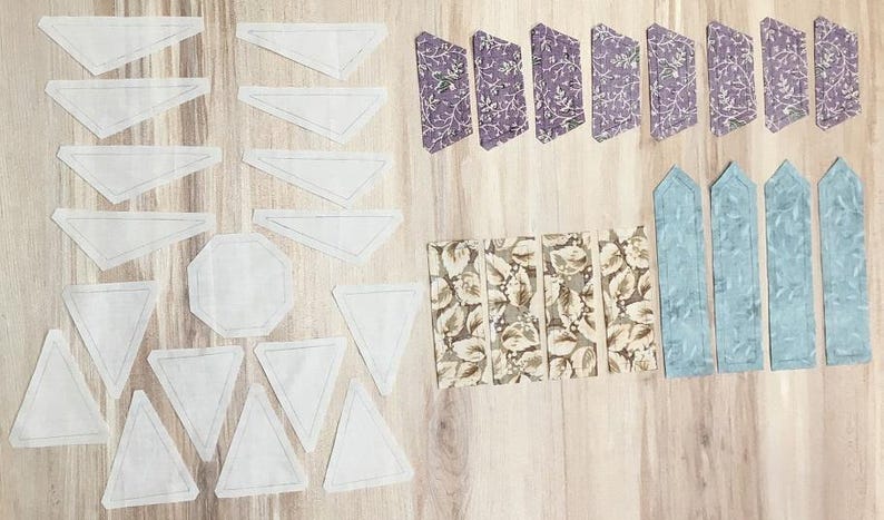 Op de afbeelding: Een verzameling stofresten in verschillende patronen en kleuren, waaronder wit, bruin, blauw en paars. De resten zijn in rijen op een houten oppervlak gerangschikt.