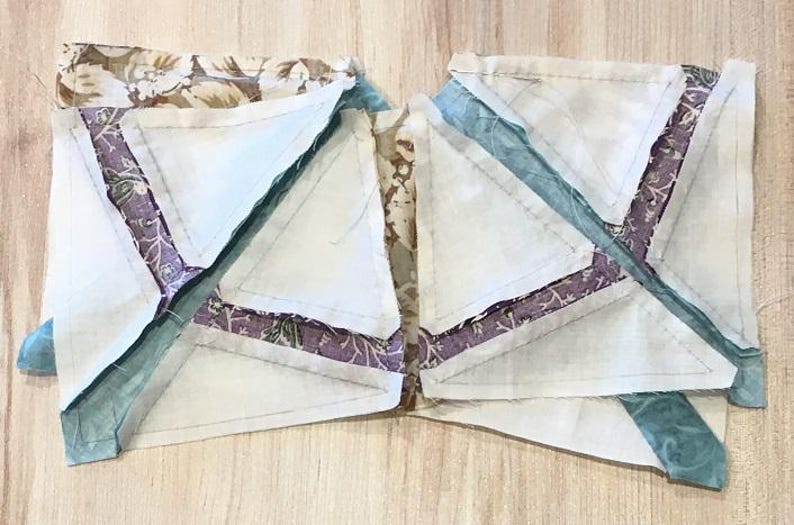 Op de afbeelding: Twee onafgewerkte quiltblokken met een witte achtergrond en verschillende stofresten in tinten paars, teal en bruin. De blokken zijn aan elkaar genaaid en hebben een stervormig ontwerp.