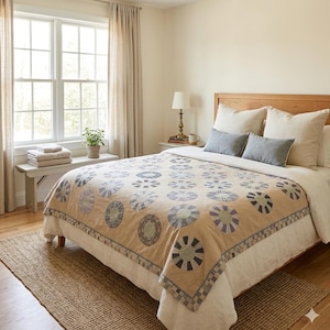 May include: A bed featuring a tan quilt with a repeating pattern of circular motifs in shades of blue, gray, and cream. The bed is dressed with two large cream-colored pillows and two smaller rectangular blue pillows, set against a wooden headboard.