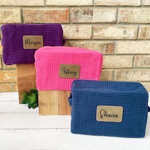 Puede incluir: Tres estuches con cremallera con nombres personalizados, "Morgan", "Tiffany" y "Shana", en morado, rosa y azul.