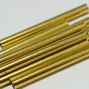 May include: A group of six gold-colored metal tubes, stacked on top of each other. The tubes are smooth and shiny.