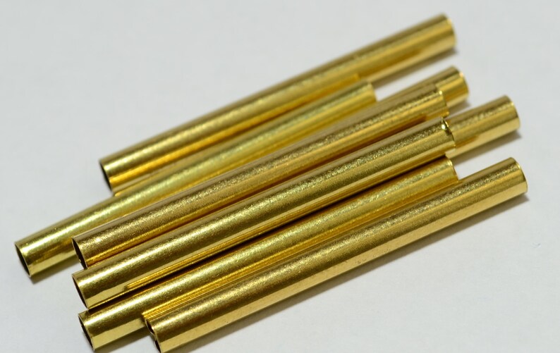 May include: A group of six gold-colored metal tubes, stacked on top of each other. The tubes are smooth and shiny.