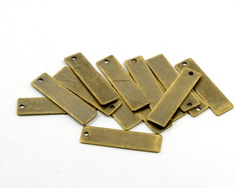 May include: A pile of antique gold-toned metal rectangular tags with a hole at the top. The tags are arranged in a random pattern.