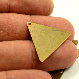 May include: A brass triangle charm with a hole at the top. The charm is a flat, geometric shape with a slightly textured surface.