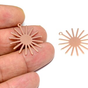 May include: Two rose gold metal sunburst charms with a hole at the top for attaching to jewelry or other crafts.