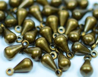 May include: A group of antique gold-toned teardrop-shaped metal charms with a loop at the top. The charms are scattered on a white surface.