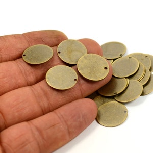 以下が含まれることがあります： 中央に穴の開いたアンティークブラス製の丸い金属ディスクの山。ディスクは手に置かれています。