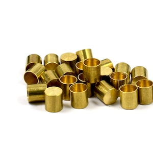 May include: A pile of small, gold-colored metal caps. The caps are cylindrical in shape and have a smooth, shiny finish.